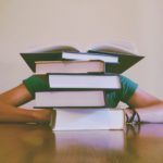 student with stack of books in front