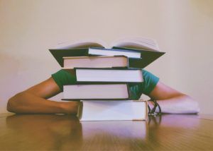 student sitting behind stack of books