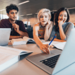 students sitting at a table and looking at a laptop