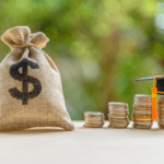 sack of money beside stacked coins with graduation hat